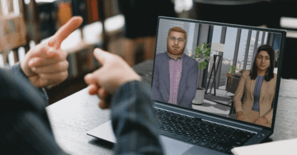 A person uses sign language in front of a laptop displaying two dynamic avatars in a virtual meeting set in a modern office environment.